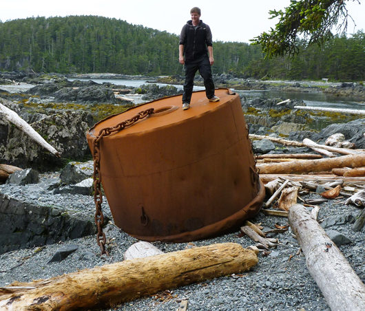 University of Alaska student Derek Chamberlin stands atop a large ship's mooring buoy which must have broken off it's chain anchor. The mooring buoy was found by NOAA marine debris scientists at Whale Bay, North Cape on Baranof Island during a recent marine debris survey of Southeast Alaska shores.