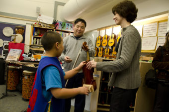 Glacier Valley Elementary music teacher Lorrie Heagy hands a student a violin as violin instructor Guo Hua Xia picks out a bow.