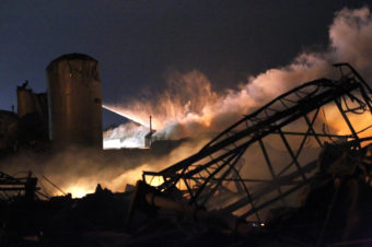Smoke rises as water is sprayed at the burning remains of the plant.