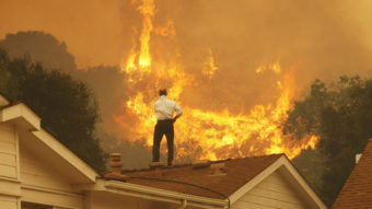 Standing on a rooftop, a man looks at the Springs fire's approaching flames in California Friday. The wildfire, reportedly, 20 percent contained, might be weakened by high humidity and cooler temperatures Saturday. David McNew/Getty Images