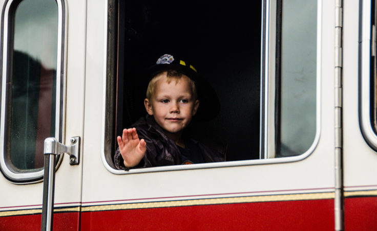 A young boy in a fireman's hat waves from the window of a Juneau fire truck.