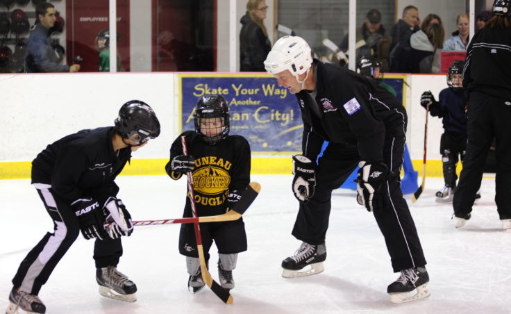 Greyson Liebelt (left) and Bill Wildes welcome a young player a few steps after he steps onto the ice at during JDIA’s Learn to Play event Saturday at Treadwell Arena.