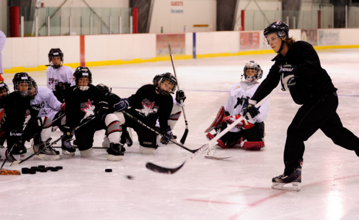 Logan Hulse demonstrates proper shooting technique while players attending the Rocky Mountain Hockey School watch in awe of his accuracy.