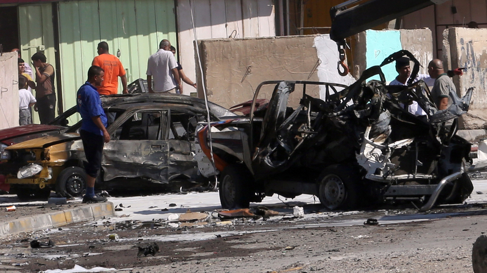 Iraqis look at the site of a car bomb attack in Baghdad, where at least 10 car bombs were detonated during the city's rush hour Monday. Khalid Mohammed/AP