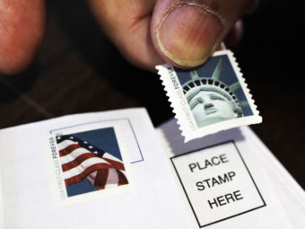 A customer places first-class stamps on envelopes at a U.S. Post Office in San Jose, Calif. It'll cost another 3 cents to send a first-class letter starting on Jan. 26. Paul Sakuma/AP