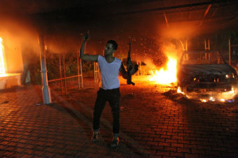 An armed man waves his arms as buildings and cars are engulfed in flames after being set on fire inside the U.S. Consulate compound in Benghazi late on Sept. 11, 2012. AFP/Getty Images