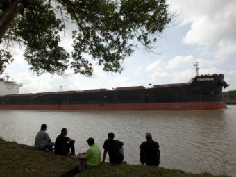 Men sit by the side of the Panama Canal as a ship sails past in Gamboa near Panama City, last month. The expansion project is aimed at accommodating the world's largest container ships. Arnulfo Franco/AP