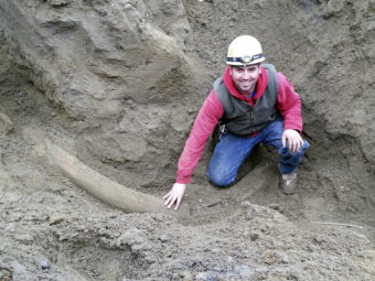 Plumber apprentice Joe Wells touching what Burke Museum officials believe is the largest, most intact mammoth tusk, ever found in the region. Uncredited/AP