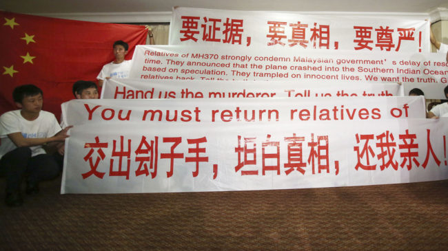 Newly arrived Chinese relatives of passengers of the missing Malaysia Airlines flight MH370 hold banners while talking to reporters at a hotel in Malaysia Sunday. The search continues for the jetliner that went missing three weeks ago. Aaron Favila/AP