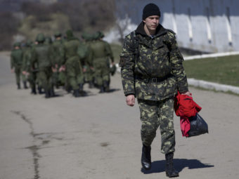 As Russian soldiers walked one way in the distance, a departing Ukrainian soldier carried some of his belongings Friday at a military base in Perevalne, Crimea. Ivan Sekretarev/AP