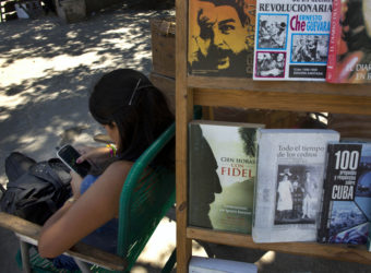A book street vendor passes the time on her smart phone as she waits for customers in Havana, Cuba, on Tuesday. The Obama administration secretly financed a social network in Cuba to stir political unrest. Ramon Espinosa/AP