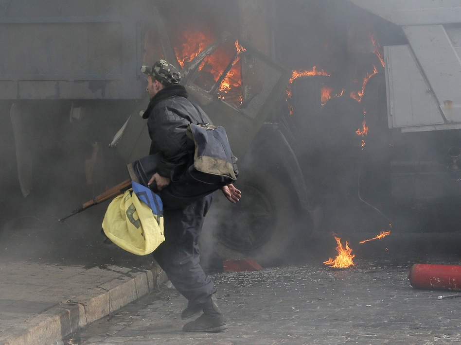 A man with a gun runs along a street during a clash between opposition protesters and riot police at a burning barricades near the Presidential office in Kiev, Ukraine, in February. Efrem Lukatsky/AP