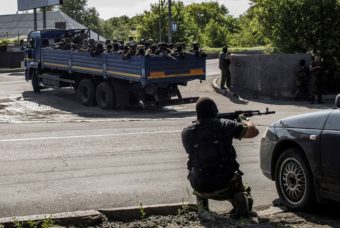 A pro-Russian fighter takes position behind a car as a truck full of rebel fighters heads toward a battle with Ukrainian forces near the airport in Donetsk Monday. The rebels say more than 30 of their number were killed in the violence. Fabio Bucciarelli/AFP/Getty Images
