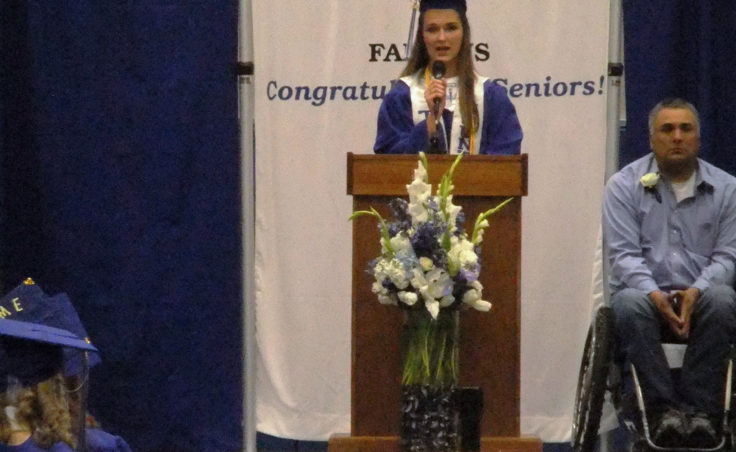 Jenna Luhrs, TMHS co-valedictorian, speaks to graduates. Assistant baseball coach Joe Tompkins is to her right. (Photo by Rosemarie Alexander/KTOO)