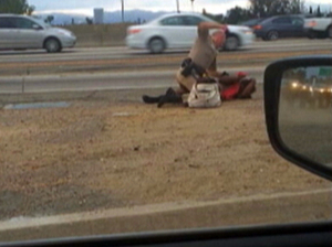 In this July 1 image from video provided by motorist David Diaz, a California Highway Patrol officer straddles a woman while punching her on the shoulder of a Los Angeles freeway. David Diaz/AP