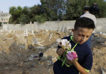 Palestinian Saeb Afana, 12, stands on the edge of a large crater from an Israeli missile strike that destroyed several graves, as he carries flowers at a cemetery in Gaza City on Monday. Lefteris Pitarakis/AP