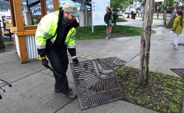 George Schaaf removes the grates from around the trees to clean up litter. (Photo by Rosemarie Alexander/KTOO)