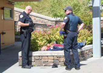 Two Juneau Police Department officers don gloves while they interact with a man lying down on Telephone Hill pocket park in July 2014. (Photo by Lisa Phu/KTOO)
