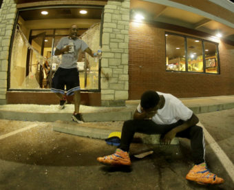 A man tries to recover from tear gas as people leave a McDonald's restaurant Sunday during a protest for Michael Brown in Ferguson, Mo. After police fired tear gas, people used bottles of water and milk to try to clear their eyes. Charlie Riedel/AP