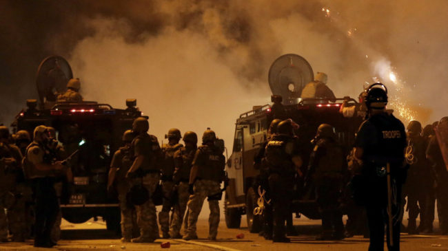 Police wait to advance after tear gas was used to disperse a crowd Sunday during a protest for Michael Brown, who was killed by a police officer last Saturday in Ferguson, Mo. Charlie Riedel/AP