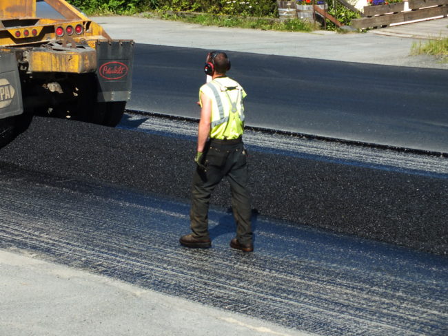 A tractor trailer returns from the asphalt plant and carefully lays down asphalt mix on top of the sprayed asphalt tack coat.(Photo by Matt Miller/KTOO)