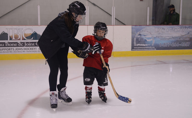 Jamie Hort shows Austin Huang how to hold a hockey stick during a Learn to Play afternoon sponsored by the Juneau Douglas Ice Association and Treadwell Ice Arena.