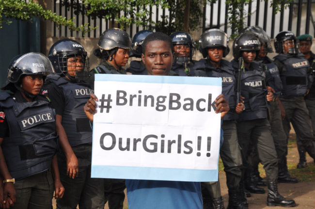 A man poses with a sign in front of police officers in riot gear during a demonstration calling on the government to rescue the kidnapped girls of a government secondary school in Chibok, in Abuja, Nigeria, on Tuesday. Olamikan Gbemiga/AP