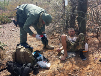 An unidentified U.S. Border Patrol agent, left, helps an immigrant, including setting up intravenous fluid replacement for dehydration, near Sells, Ariz. on June 25. (Astrid Galvan/AP)