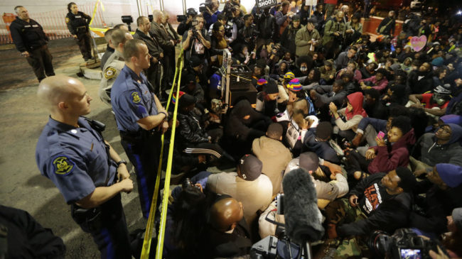 Protesters sit silently for over four minutes at the Ferguson Police Department Saturday, during a rally in remembrance of Michael Brown in Ferguson, Mo. While the demonstration was peaceful, police arrested protesters elsewhere. Charles Rex Arbogast/AP