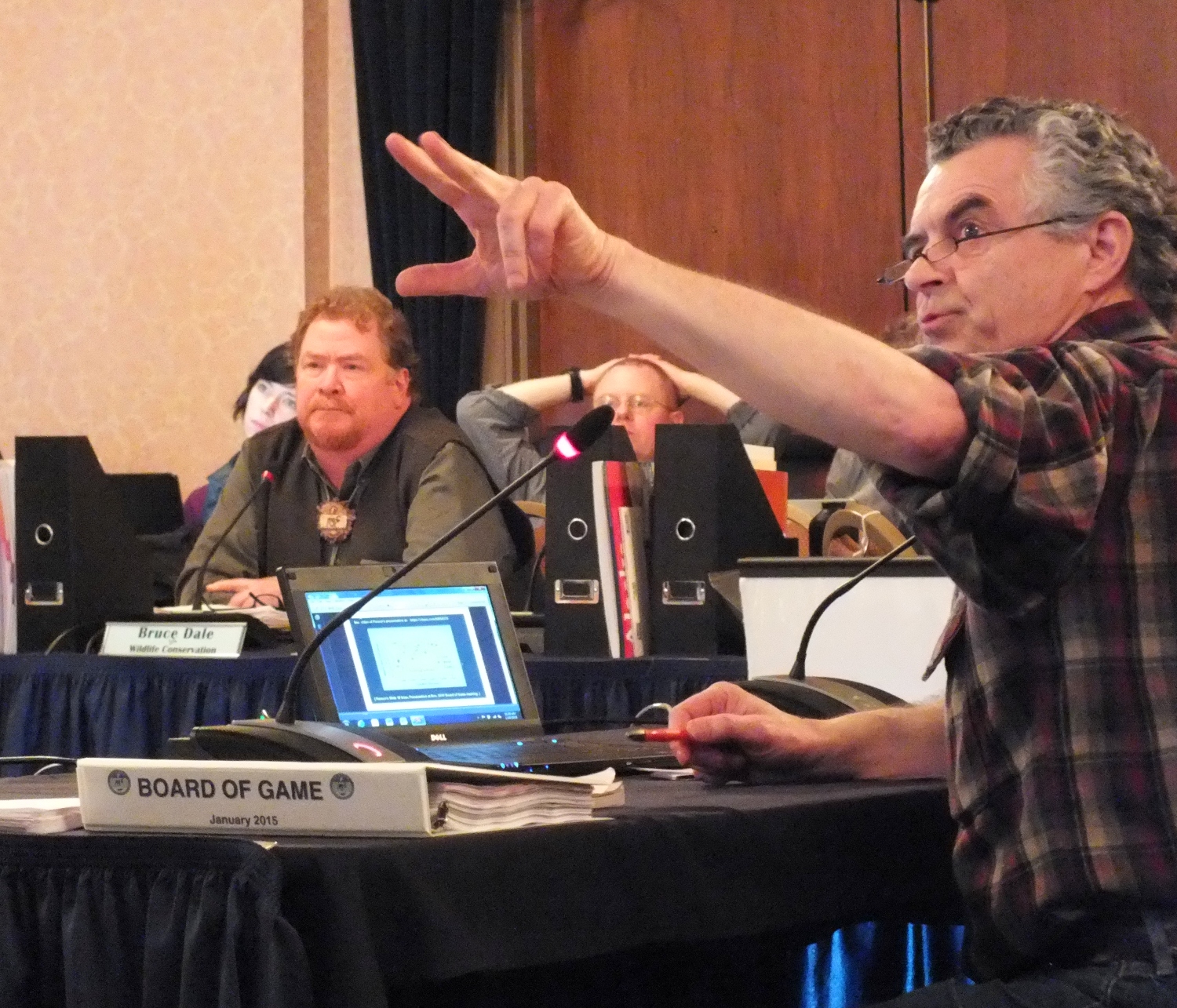 Larry Edwards of Greenpeace (right) points to an overhead projection of a slide while providing testimony on a proposal to limit wolf harvest on Prince of Wales Island as Bruce Dale, acting Director of Division of Wildlife Conservation, listens during the Board of Game's meeting in Juneau on Jan. 9, 2015. (Photo by Matt Miller/KTOO)