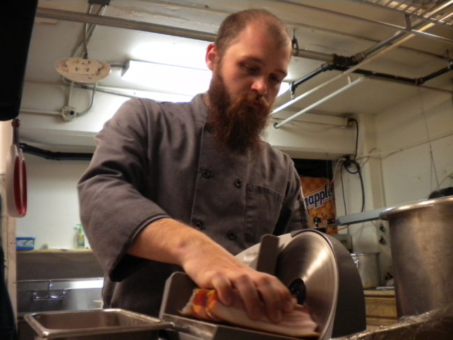Brian Keeney, kitchen manager of V's Cellar Door, slices bacon for one of the dishes the restaurant is entering in Baconfest. (Photo by Kevin Reagan/ KTOO)