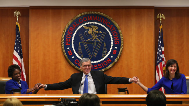 At the start of a meeting to decide the issue of net neutrality, Federal Communications Commission Chairman Tom Wheeler (center) holds hands with FCC Commissioners Mignon Clyburn (left) and Jessica Rosenworcel at the FCC headquarters Thursday.