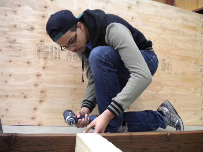 Juneau Douglas High School junior Malik Jones works on a wooden frame that will be part of a mobile greenhouse project. (Photo by Kevin Reagan / KTOO)