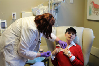 Anne Koller closes her eyes as an oncology nurse attaches a line for chemotherapy to a port in her chest. Koller typically spends 3 to 6 hours getting each treatment. (Photo by Sarah Jane Tribble/WCPN)