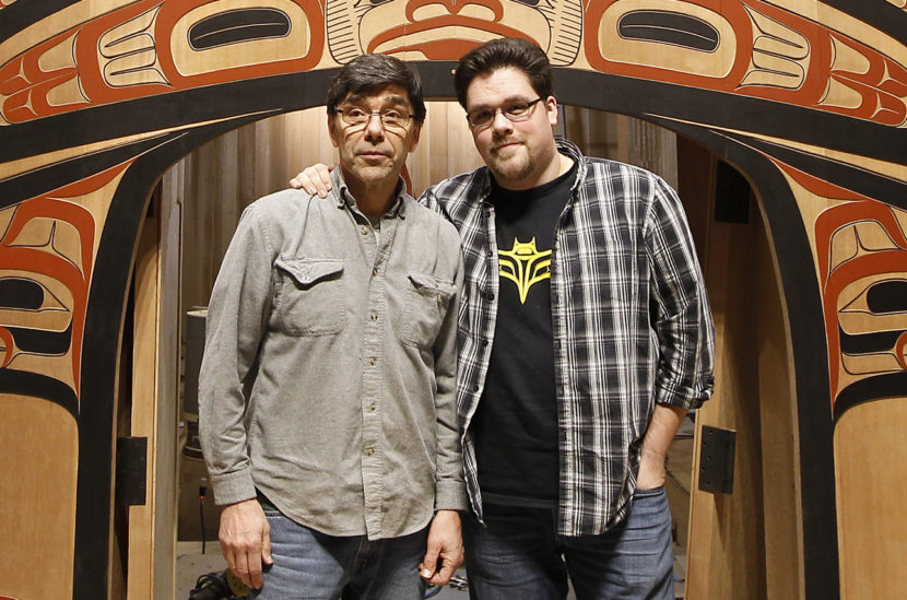 Two men stand in front of the carved and painted front of a building