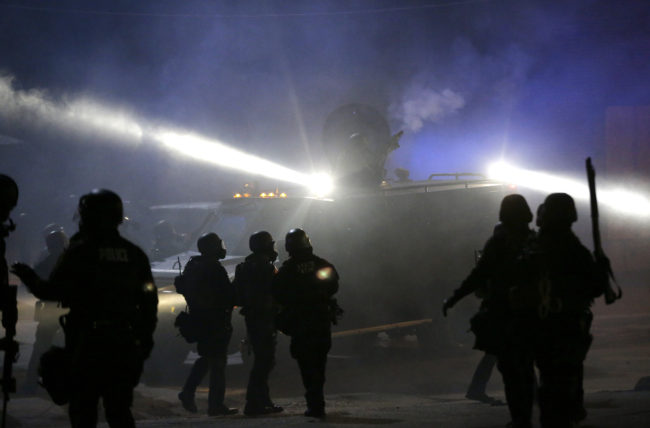 Police in riot gear stand around an armored vehicle as smoke fills the streets of Ferguson, Mo., in November 2014. Charlie Riedel/AP