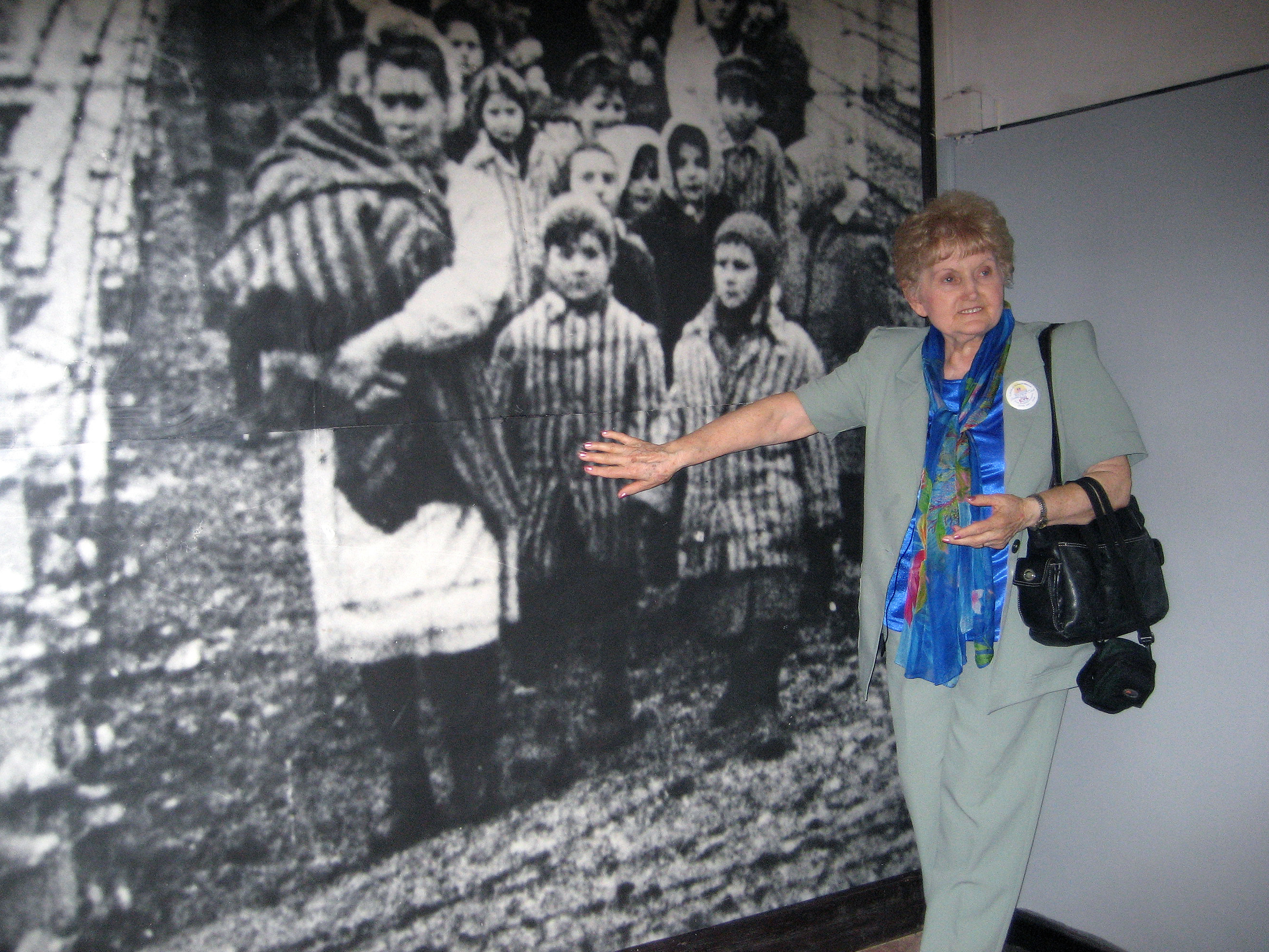 Eva Kor points to an image of herself on the wall of the Auschwitz-Birkenau State Museum in Poland. Courtesy of the CANDLES Holocaust Museum and Education Center