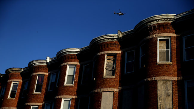 A helicopter flies over a section of Baltimore affected by riots. Richard Rothstein writes that recent unrest in Baltimore is the legacy of a century of federal, state and local policies designed to "quarantine Baltimore's black population in isolated slums." Patrick Smith/Getty Images
