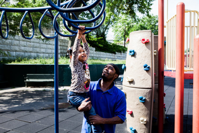Shakir Everett helps his niece, Janai Williams, 2, across the monkey bars at Mildred Helms Park in Newark. The playground is an asset in the daytime, but a "terror zone" at night, with drug and gang activity, neighbors say. Alex Welsh for NPR