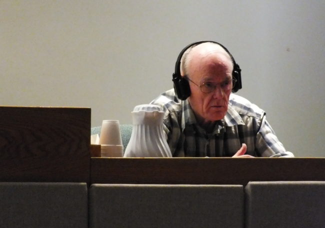 Rayco Sales owner Ray Coxe wears a set of hearing-assist headphones as he listens to a question  in Juneau Superior Court on Wednesday. (Photo by Matt Miller)