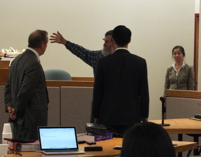 Landscaper Ed Buyarski demonstrates what happened when Simone Kim was shot on the east side of the Fred Meyer store on Aug. 4, 2006. Sun Hee Choate (right) stands at the approximate location of landscaping assistant Alex Satre while attorney Jon Choate (center, back turned) is where Kim was standing. Attorney Mark Choate (left) is standing where Jason Coday walked up to Kim and shot him with a sawed-off rifle. (Photo by Matt Miller/KTOO)