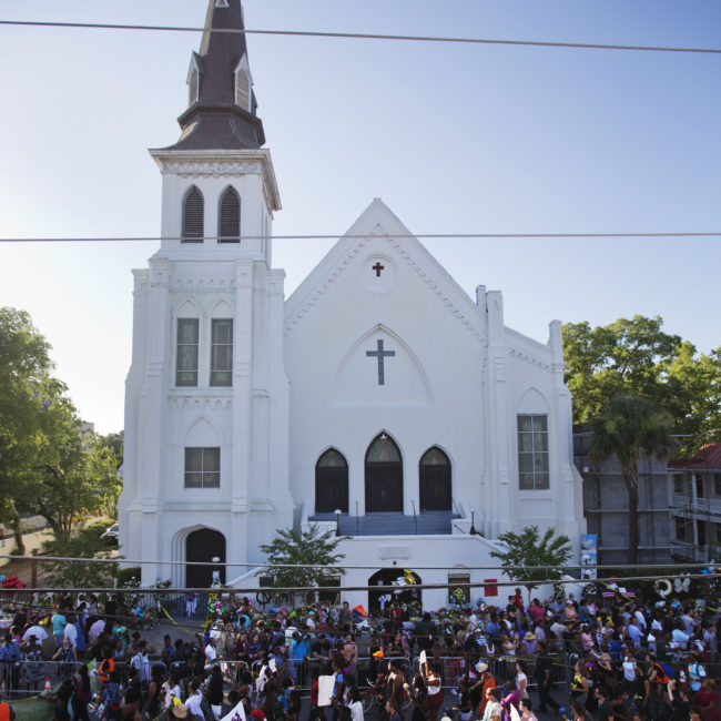 A remembrance march in memory of the Emanuel AME Church shooting victims passes a sidewalk memorial in front of the church on Saturday. The church today will hold its first Sunday service since Wednesday's shooting. David Goldman/AP