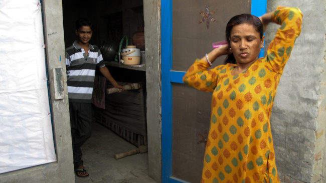Saroj's teenage son watches her comb her hair before she heads to work. Rhitu Chatterjee for NPR