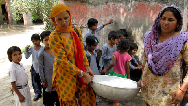 Saroj (left) helps her colleague carry a cauldron of rice to the school kitchen after washing it. Rhitu Chatterjee for NPR