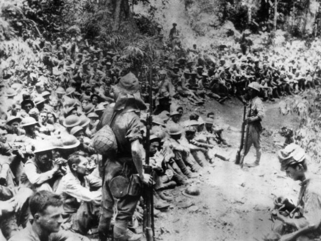 In this 1942 file photo provided by the U.S. Marine Corps, Japanese soldiers stand guard over American prisoners of war just before the start of the Bataan Death March following the Japanese occupation of the Philippines. Some of those who survived the death march were later forced to work for Japanese industry. 