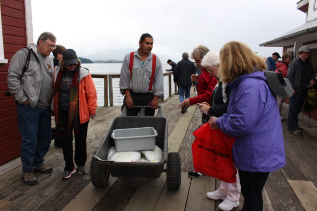 An employee in uniform answers tourists questions about halibut being wheeled around the boardwalk. (Photo by Elizabeth Jenkins/KTOO)