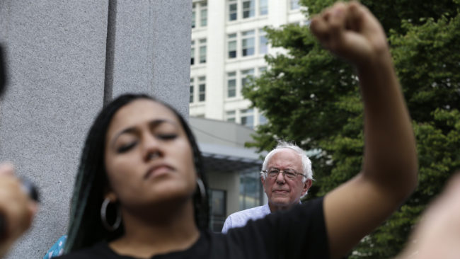 Mara Jacqueline Willaford, left, holds her fist overhead as Democratic presidential candidate Sen. Bernie Sanders, I-Vt., stands nearby at a rally Saturday. The activists took over the microphone and refused to allow Sanders to speak. Elaine Thompson/AP