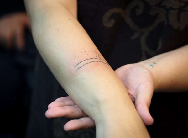 Holly Mititquq Nordlum shows off her partially complete tattoo during a live demonstration at Anchorage’s Above The Rest studio. Each horizontal line is 40 individual stitch marks through the first layer of skin. Before starting the stitches, Jacobsen poked the basic design of three bird feet rising from the lines. Nordlum’s Inupiaq name, Mititquq, means ‘a place where birds land,’ and she celebrates big life goals with bird feet tattoos, like the two on her opposite wrist, done with a tattoo gun. (Photo by Zachariah Hughes/ KSKA)