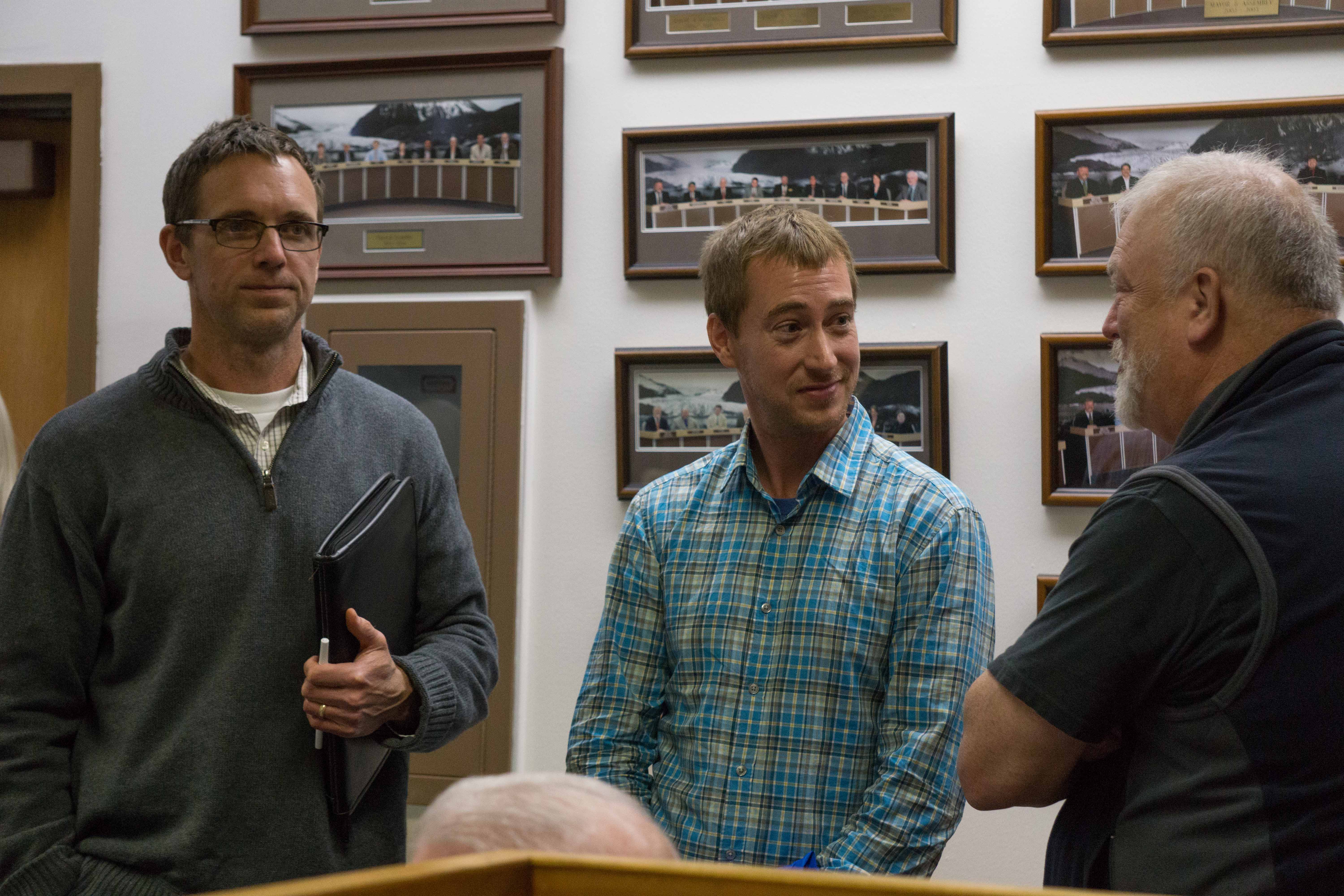 Avista's Jeff Smith, left, and AELP's Eric Eriksen, center chat with Bruce Botelho at the Juneau Assembly's Committee of the Whole meeting. (Photo by Jeremy Hsieh/KTOO)