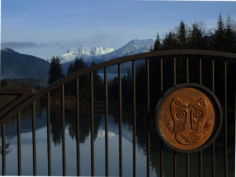 Glass-smooth Mendenhall River, Mendenhall Glacier, and the Juneau Icefield form the backdrop for one of the bronze medallions designed by Roy Peratovich Jr. Tlingit moieties Eagle and Raven stand upon a rock that represents the Alaska Native Brotherhood. (Photo by Matt Miller/KTOO)